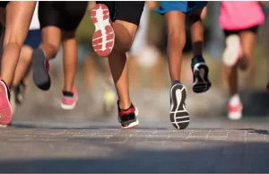 Corredores en movimiento durante una maratón, con enfoque en los pies y zapatillas deportivas sobre el asfalto.